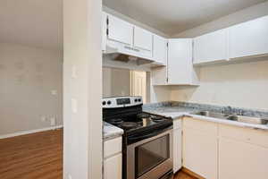 Kitchen featuring electric range, under cabinet range hood, a sink, dark wood-style floors, and light countertops