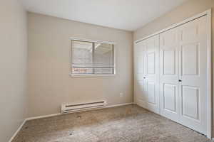 Unfurnished bedroom featuring baseboard heating, carpet flooring, a closet, and baseboards