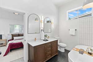 Owners Suite: Ensuite bathroom featuring a freestanding tub, double vanity, baseboards, and toilet