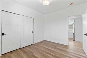 Unfurnished bedroom with light wood-style floors, baseboards, stainless steel refrigerator, and a closet