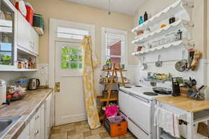 Kitchen featuring white electric range oven, open shelves, a wainscoted wall, white cabinets, and stone finish floors