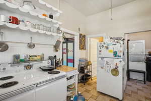 Kitchen featuring white appliances, stacked washing machine and dryer, and stone tile flooring