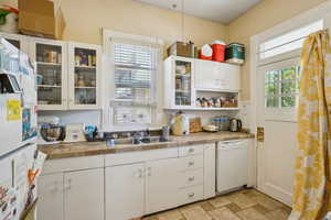 Kitchen with white appliances, white cabinetry, a sink, glass insert cabinets, and stone finish floors