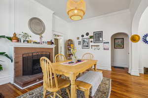 Dining area with arched walkways, crown molding, wood finished floors, a brick fireplace, and baseboards