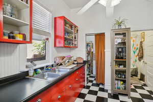 Kitchen with tile patterned floors, red cabinetry, a sink, and dark countertops