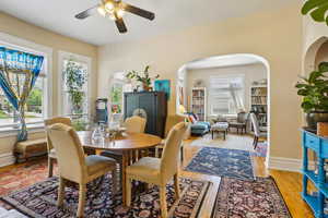 Dining room with ceiling fan, arched walkways, light wood-style floors, and baseboards