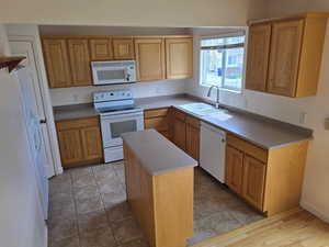 Kitchen featuring white appliances, a sink, a kitchen island, and light countertops