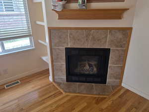 Detailed view of wood finished floors, a tiled fireplace, and baseboards