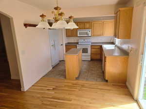 Kitchen with white appliances, a sink, a kitchen island, light wood-type flooring, and a chandelier