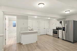 ADU kitchen featuring appliances with stainless steel finishes, a sink, a peninsula, light wood-type flooring, and light countertops