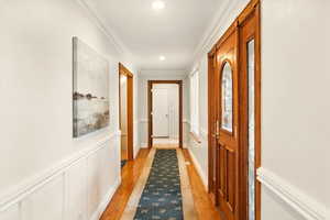 Doorway to outside with light wood-style floors, ornamental molding, recessed lighting, and wainscoting