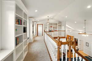 Balcony hallway featuring an upstairs landing, vaulted ceiling, recessed lighting, built-in bookcases, and light colored carpet