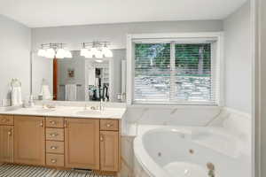 Primary full bath featuring healthy amount of natural light, a jetted tub, and double vanity