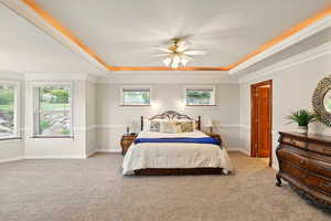 Bedroom featuring a tray ceiling, light colored carpet, crown molding, and multiple windows