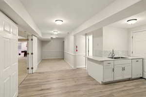 ADU living area and kitchen featuring a sink, white dishwasher, light wood-style floors, decorative backsplash, and white cabinetry