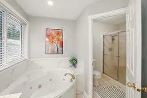 Primary bathroom with a shower stall, tile patterned flooring, a tub with jets, and toilet