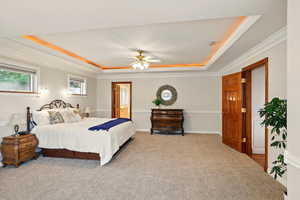 Bedroom with a raised ceiling, carpet flooring, crown molding, connected bathroom, and a ceiling fan