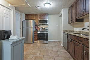Kitchen featuring stainless steel appliances, a sink, baseboards, a textured ceiling, and light stone countertops