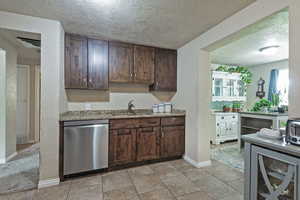 Kitchen featuring stainless steel dishwasher, a sink, a textured ceiling, baseboards, and light stone counters