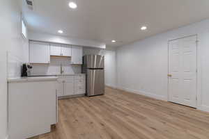 Kitchen featuring freestanding refrigerator, white cabinetry, light countertops, light wood-type flooring, and backsplash