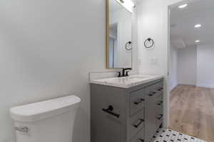 Half bathroom with recessed lighting, vanity, toilet, and wood finished floors