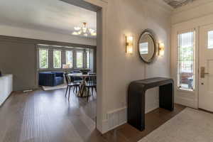 Entrance foyer with wood finished floors, a chandelier, ornamental molding, and baseboards