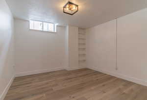 Basement with light wood-style floors, baseboards, and a textured ceiling