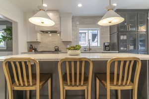 Kitchen with backsplash, white cabinets, glass insert cabinets, light stone countertops, and recessed lighting