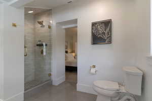 Bathroom featuring toilet, a stall shower, tile patterned floors, connected bathroom, and baseboards