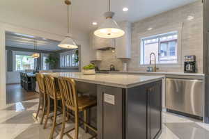Kitchen with stainless steel dishwasher, a center island, tasteful backsplash, white cabinets, and a breakfast bar area