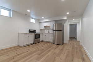 Kitchen featuring stainless steel appliances, a sink, white cabinets, decorative backsplash, and light countertops