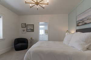 Carpeted bedroom with a chandelier, connected bathroom, and baseboards
