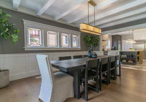 Dining space with beam ceiling, wood-type flooring, a decorative wall, and a wainscoted wall