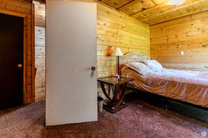 Bedroom with wooden ceiling, wooden walls, and carpet