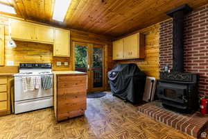 Kitchen with white electric range oven, a wood stove, wooden walls, and wood ceiling