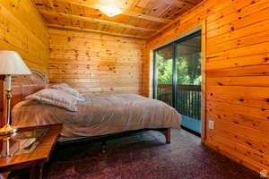 Bedroom with wood ceiling, wooden walls, access to outside, and carpet floors