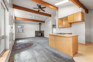 Kitchen featuring a wood stove, beam ceiling, a ceiling fan, white stovetop, and open floor plan