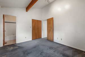 Unfurnished bedroom featuring beamed ceiling, baseboards, carpet, connected bathroom, and high vaulted ceiling