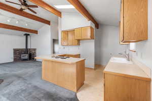 Kitchen featuring a sink, white electric stovetop, a ceiling fan, a wood stove, and light countertops