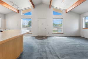 Carpeted foyer entrance featuring beam ceiling, track lighting, high vaulted ceiling, and baseboards