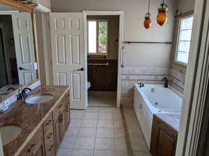 Bathroom featuring healthy amount of natural light, tile walls, toilet, a whirlpool tub, and wainscoting