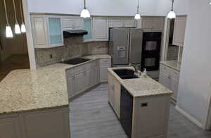 Kitchen featuring black appliances, a sink, under cabinet range hood, backsplash, and light wood-type flooring
