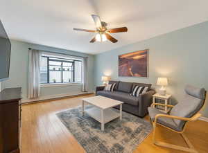 Living area featuring baseboard heating, light wood-style flooring, and a ceiling fan
