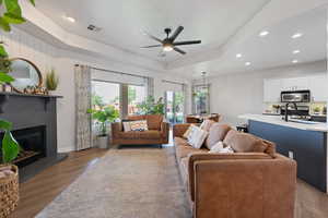 Living area featuring recessed lighting, wood finished floors, a ceiling fan, a raised ceiling, and a fireplace