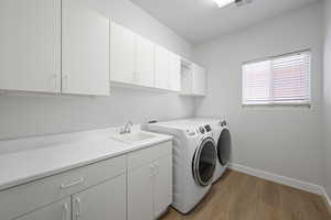 Laundry area with cabinet space, light wood finished floors, washer and dryer, and baseboards