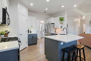 Kitchen featuring a sink, black microwave, stainless steel refrigerator with ice dispenser, a kitchen bar, and a peninsula
