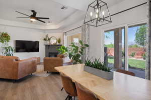 Dining space featuring wood finished floors, a ceiling fan, a chandelier, and a glass covered fireplace