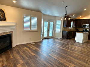 Kitchen with appliances with stainless steel finishes, a sink, dark brown cabinetry, dark wood-style flooring, and baseboards