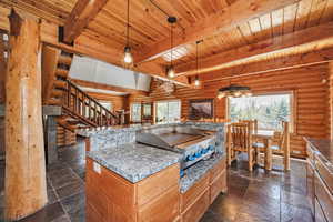 Kitchen featuring rustic walls, beamed ceiling, wooden ceiling, stone tile floors, and open floor plan