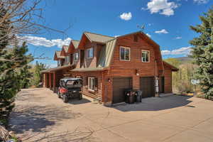 View of home's exterior featuring concrete driveway, a garage, metal roof, log exterior, and a gambrel roof